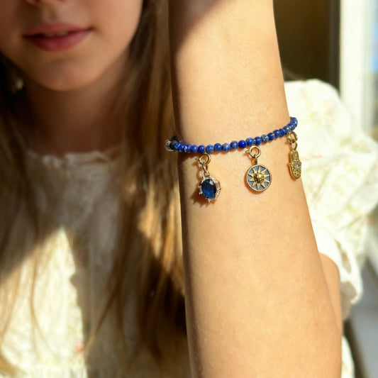 Close-up of a person's arm wearing a blue crystal lapis lazuli beaded bracelet with golden charms.