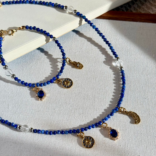 Blue crystal beaded necklace and bracelet jewelry set with gold charms on a white surface