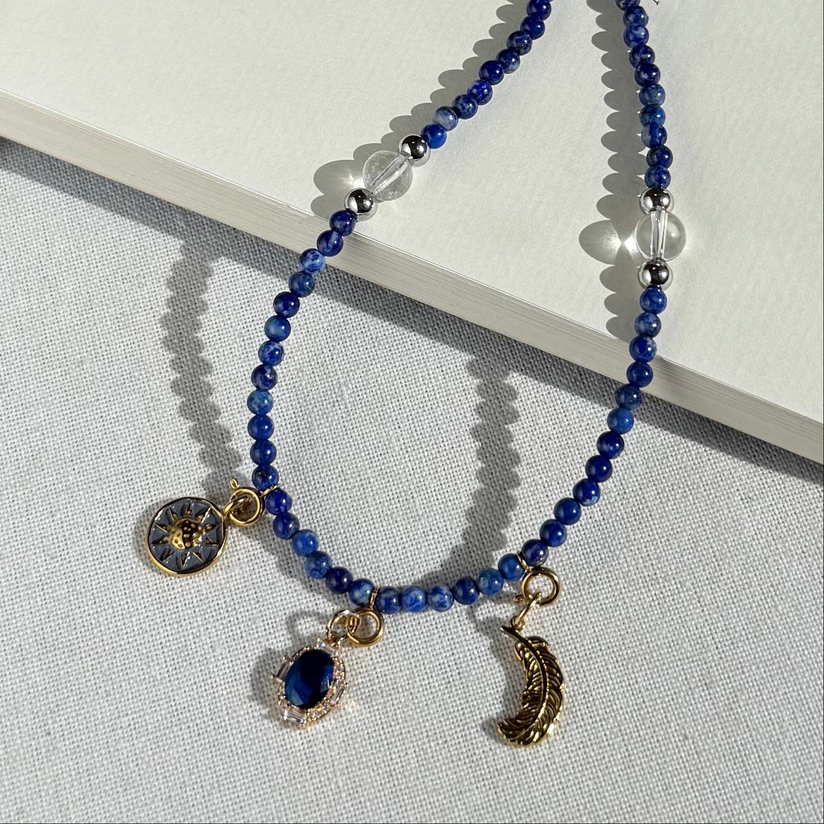 Blue beaded lapis lazuli crystal necklace with gold charms on a book
