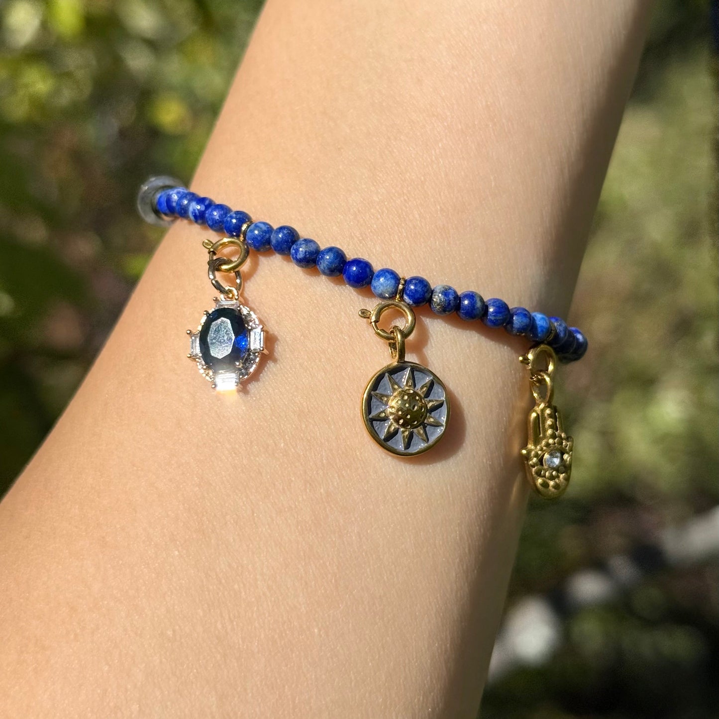 Bracelet with blue lapis lazuli beads and charms on a wrist against a blurred natural background