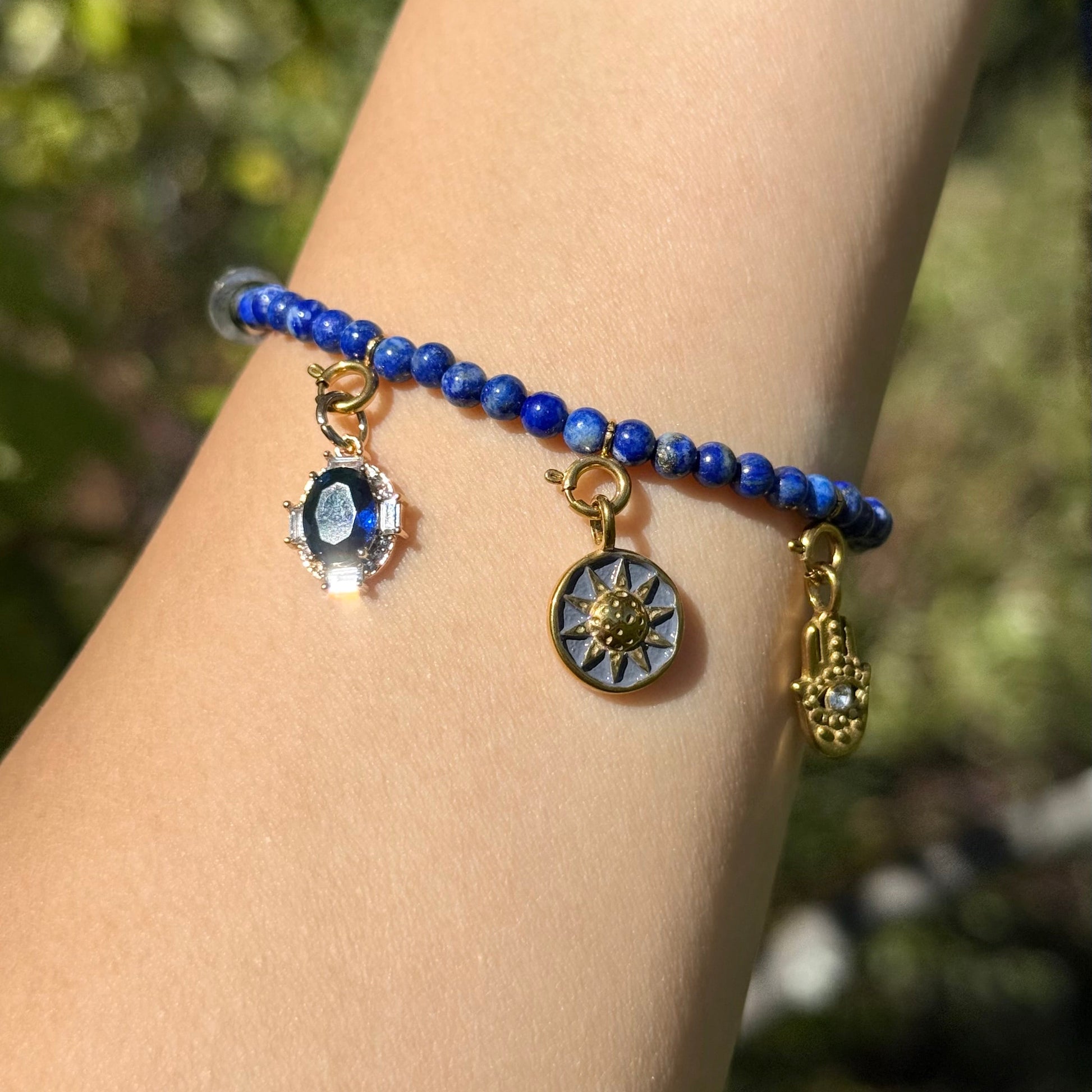Bracelet with blue lapis lazuli beads and charms on a wrist against a blurred natural background