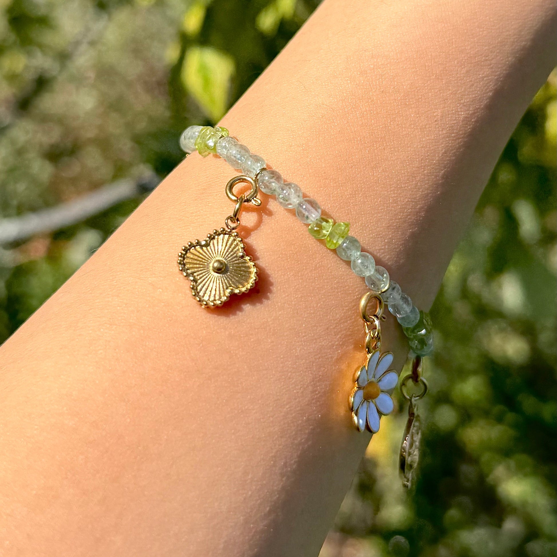 Green crystal bracelet with floral charm on a wrist against a blurred green background