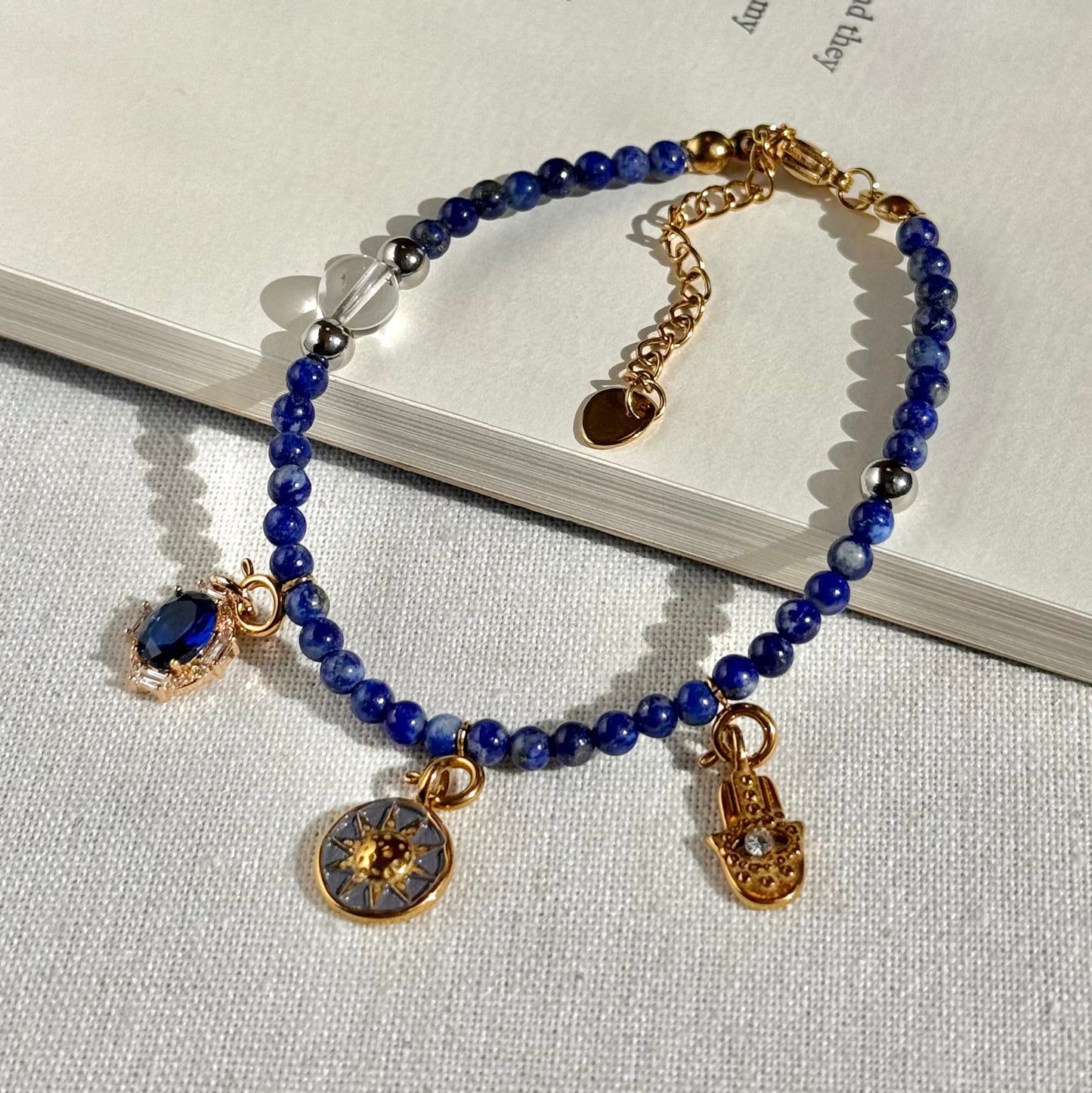 Blue Lapis Lazuli beaded bracelet with gold charms on a textured surface