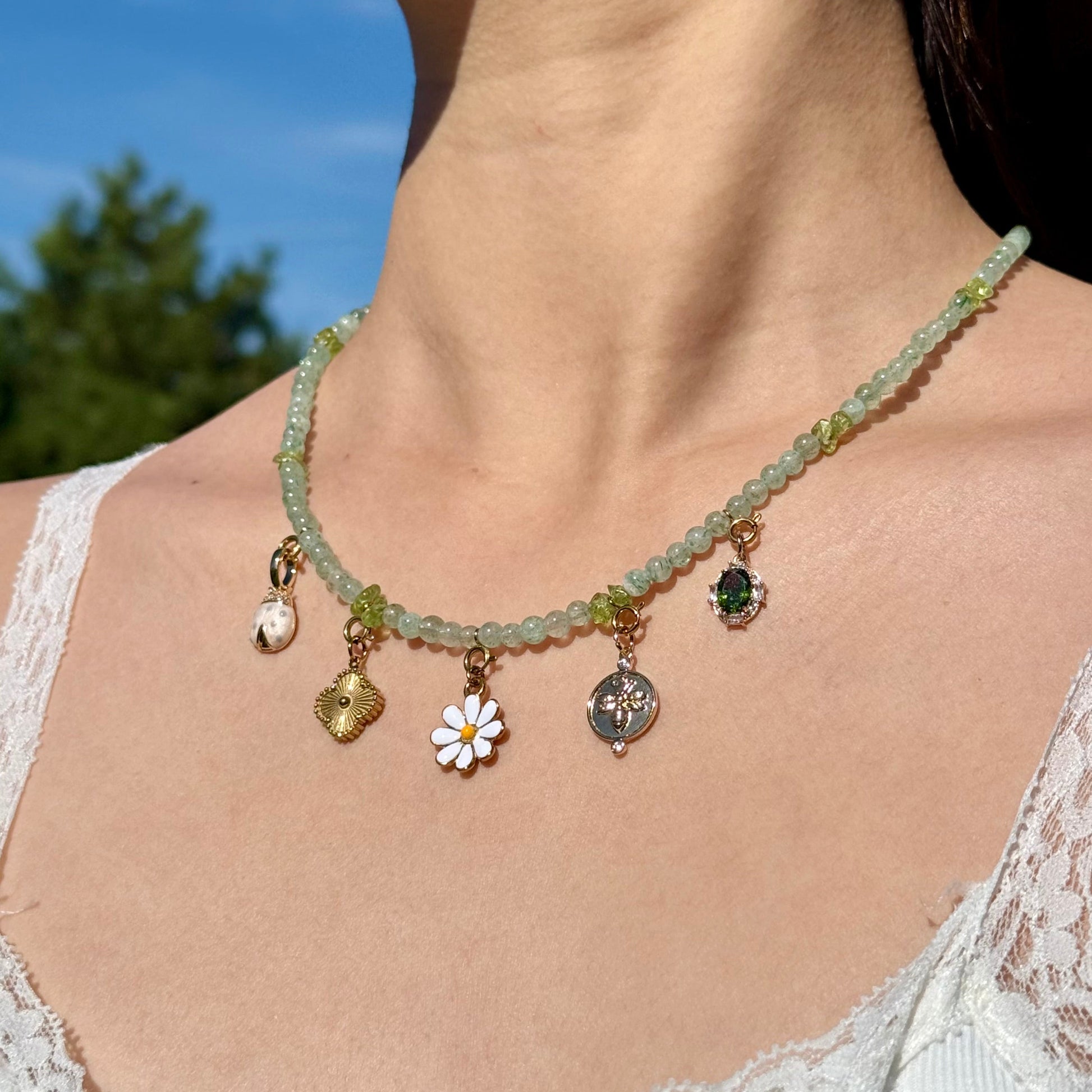 Green aventurine and peridot beaded necklace with various golden charms worn by a person against a blurred natural background