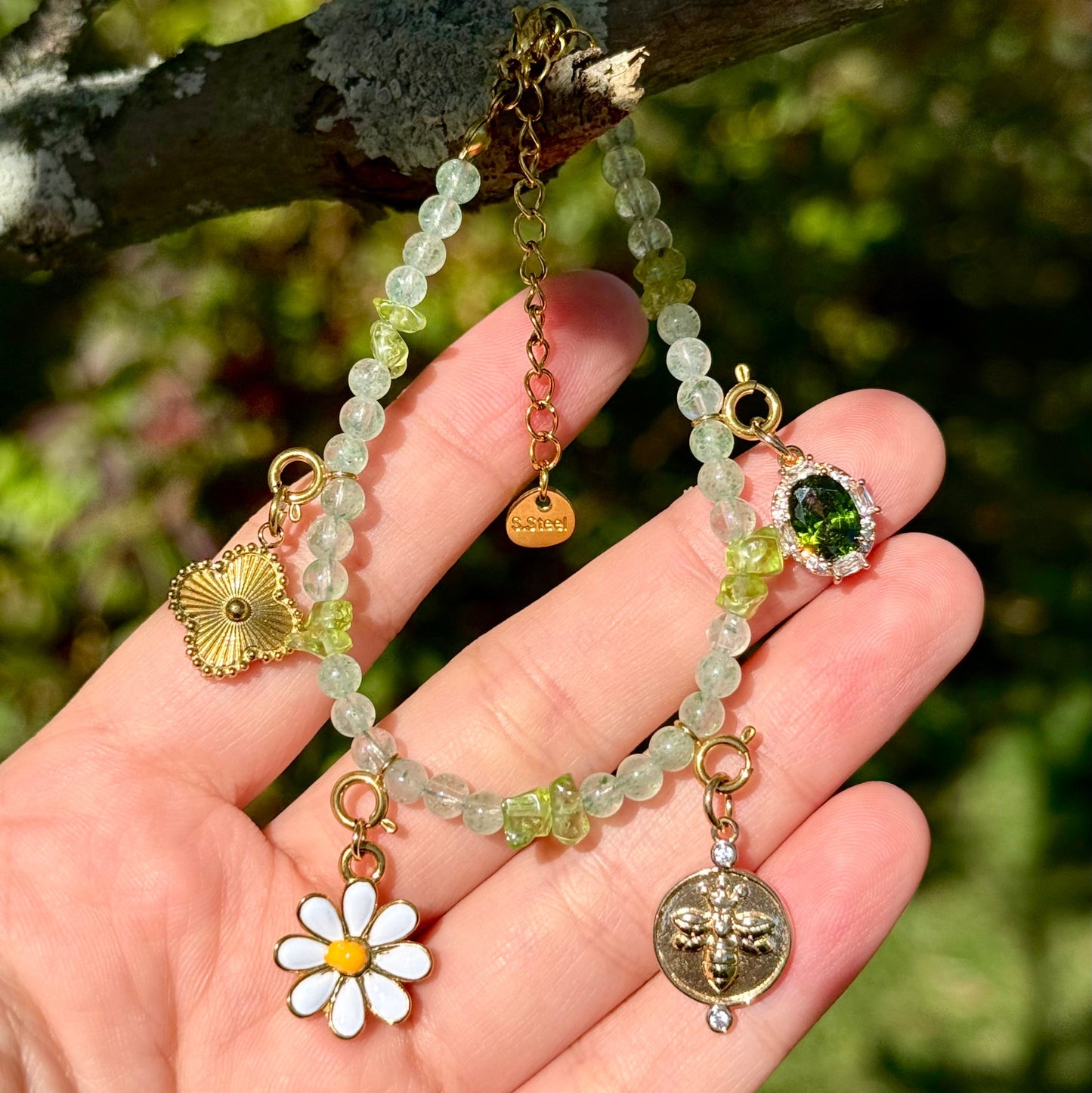 Green Aventurine and peridot beaded bracelet with various golden charms against a natural background