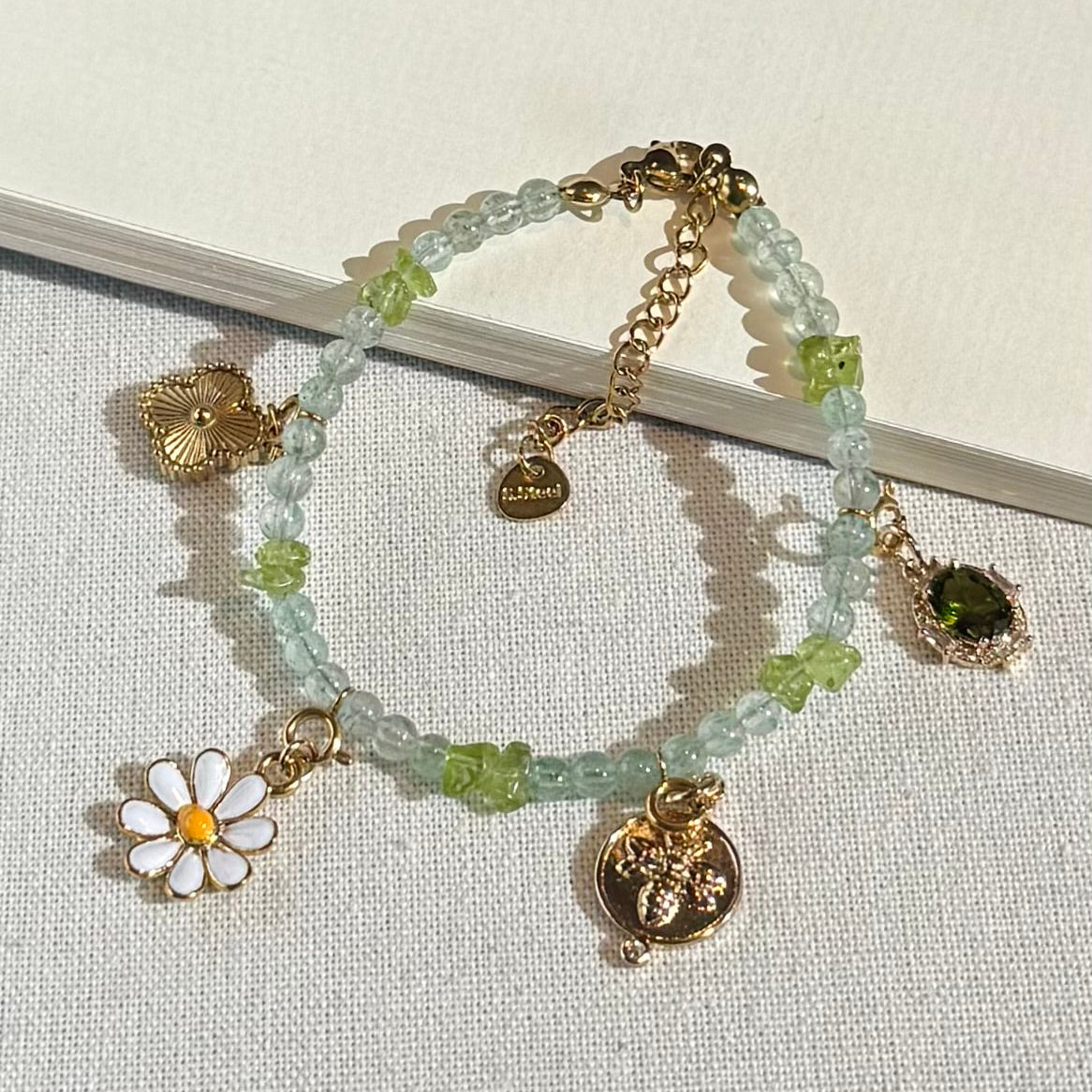 Green crystal stone Bracelet with various gold charms including a flower and gold accents on a light background