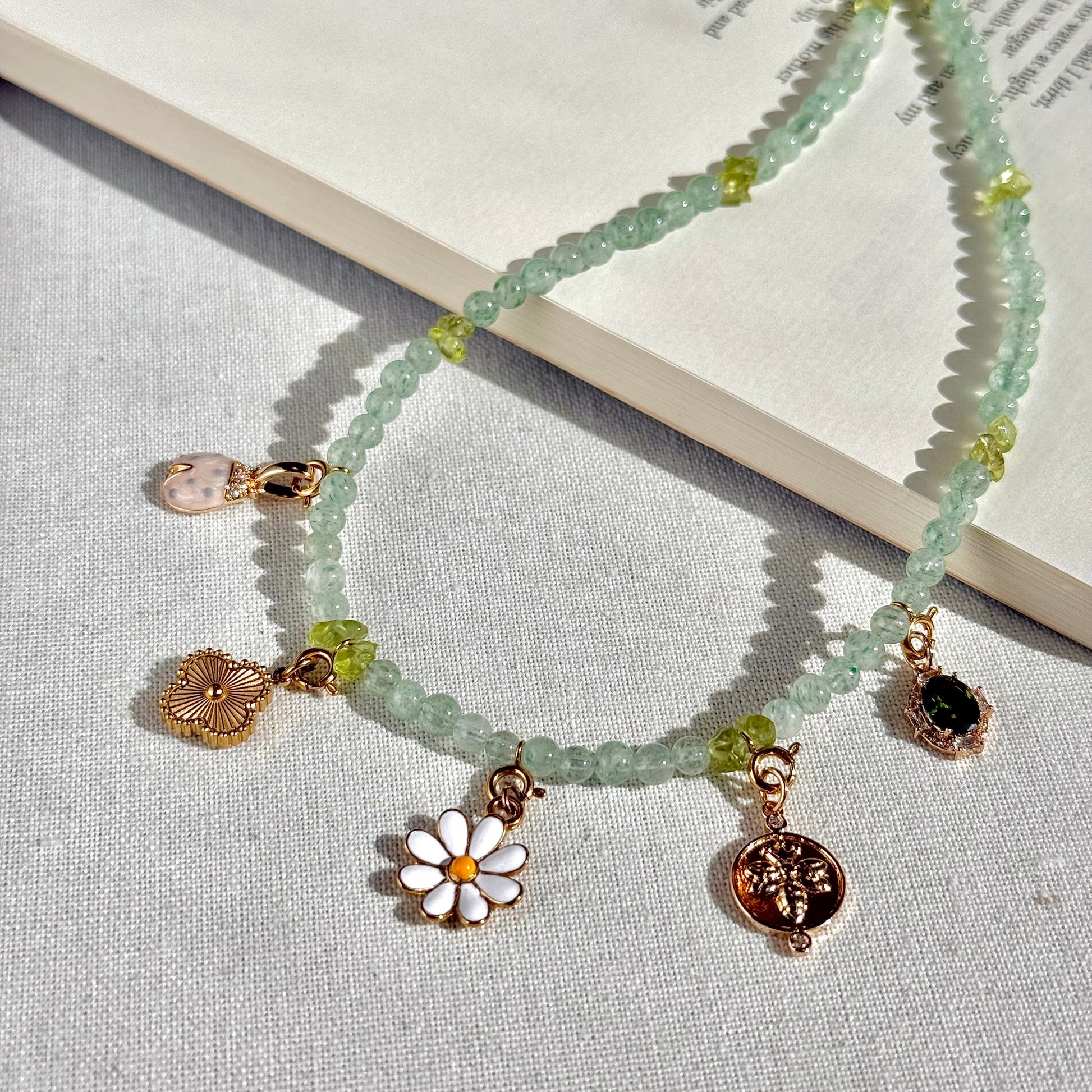 Green aventurine and peridot Necklace with various charms on a textured surface