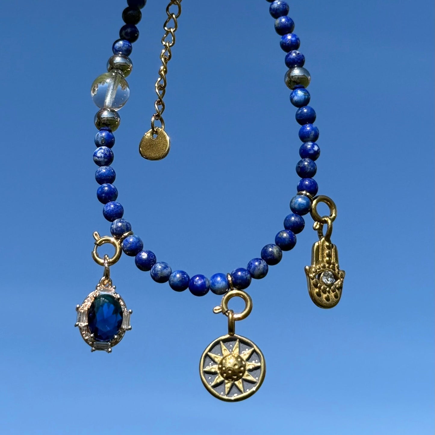 Blue lapis lazuli beaded bracelet with gold charms against a clear blue sky