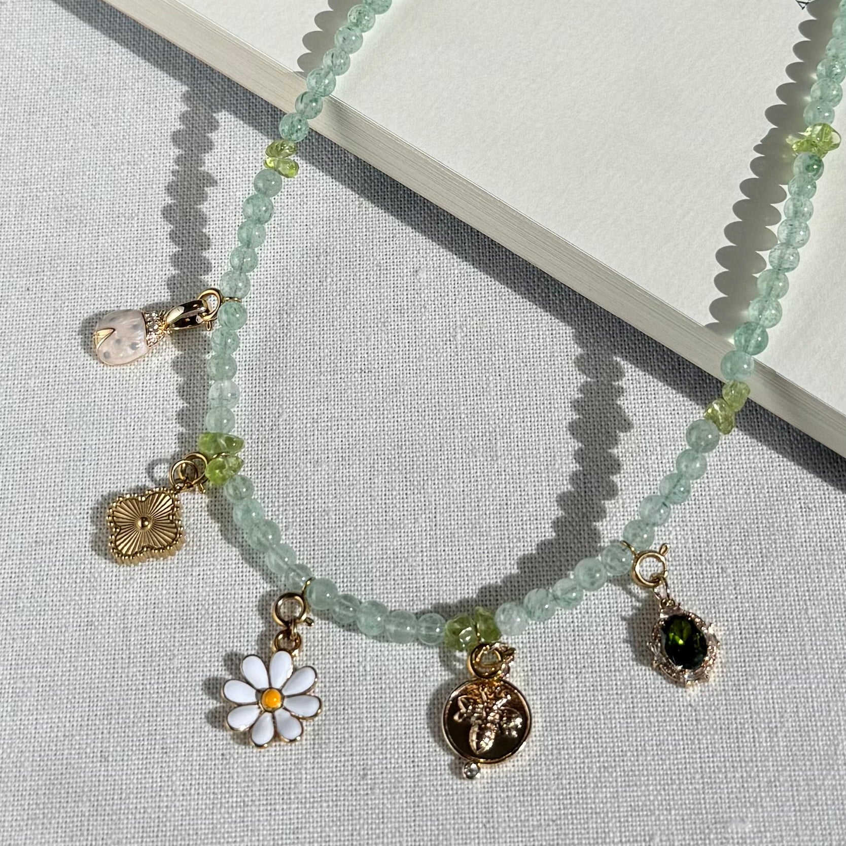 Green Crystal Necklace with various golden charms on a textured surface