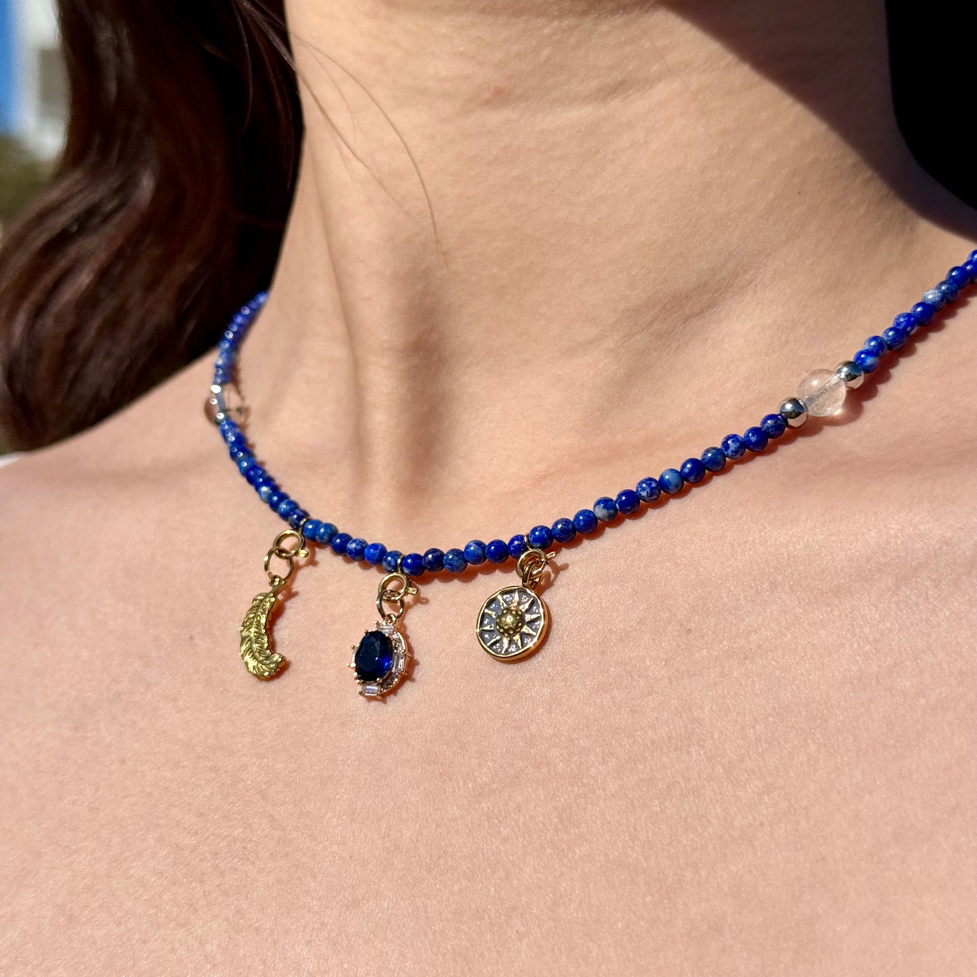 Close-up of a blue lapis lazuli beaded necklace with golden celestial charms on a person's neck.
