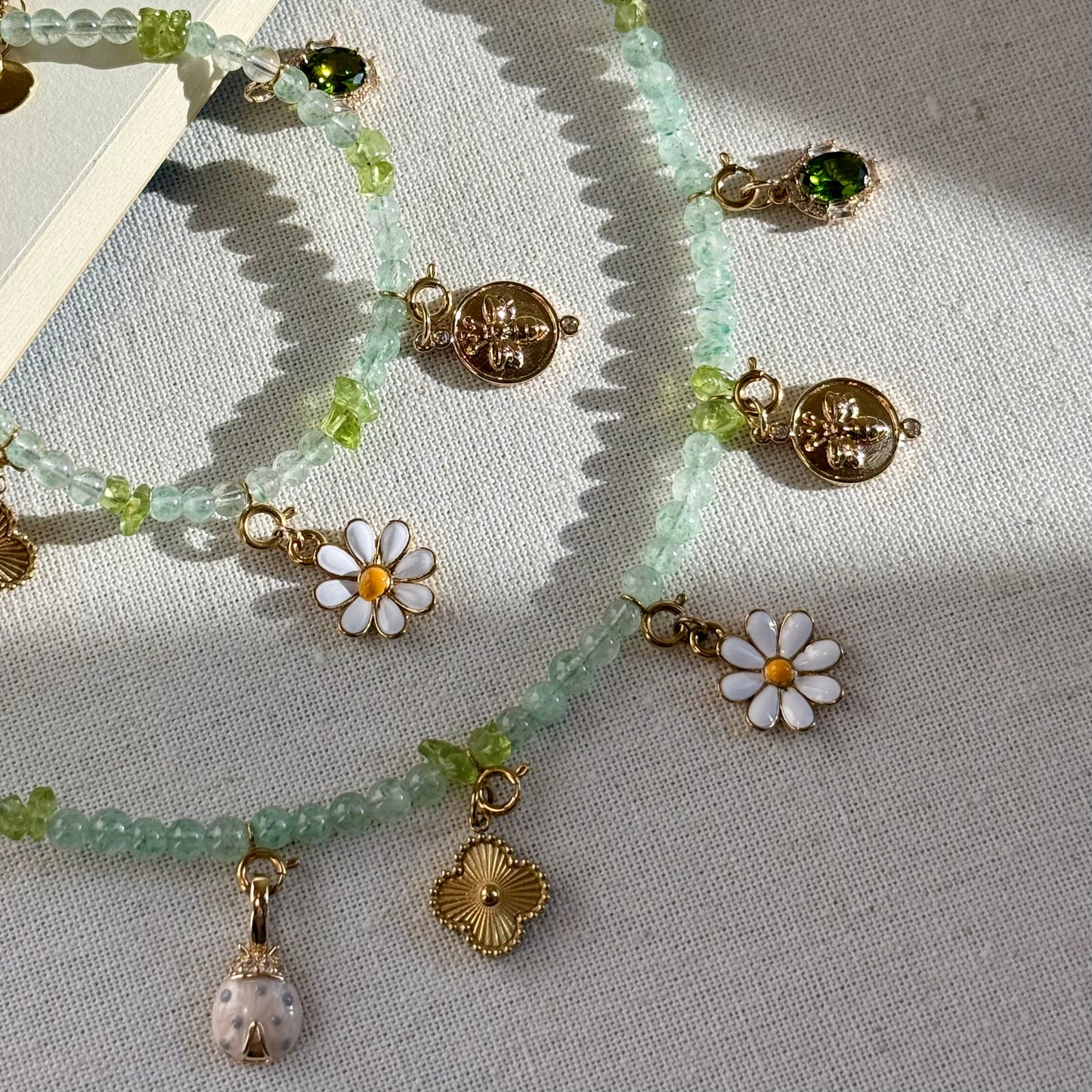 Zoom-in Necklace and bracelet set with green beads and golden floral forest bee charms on a textured surface