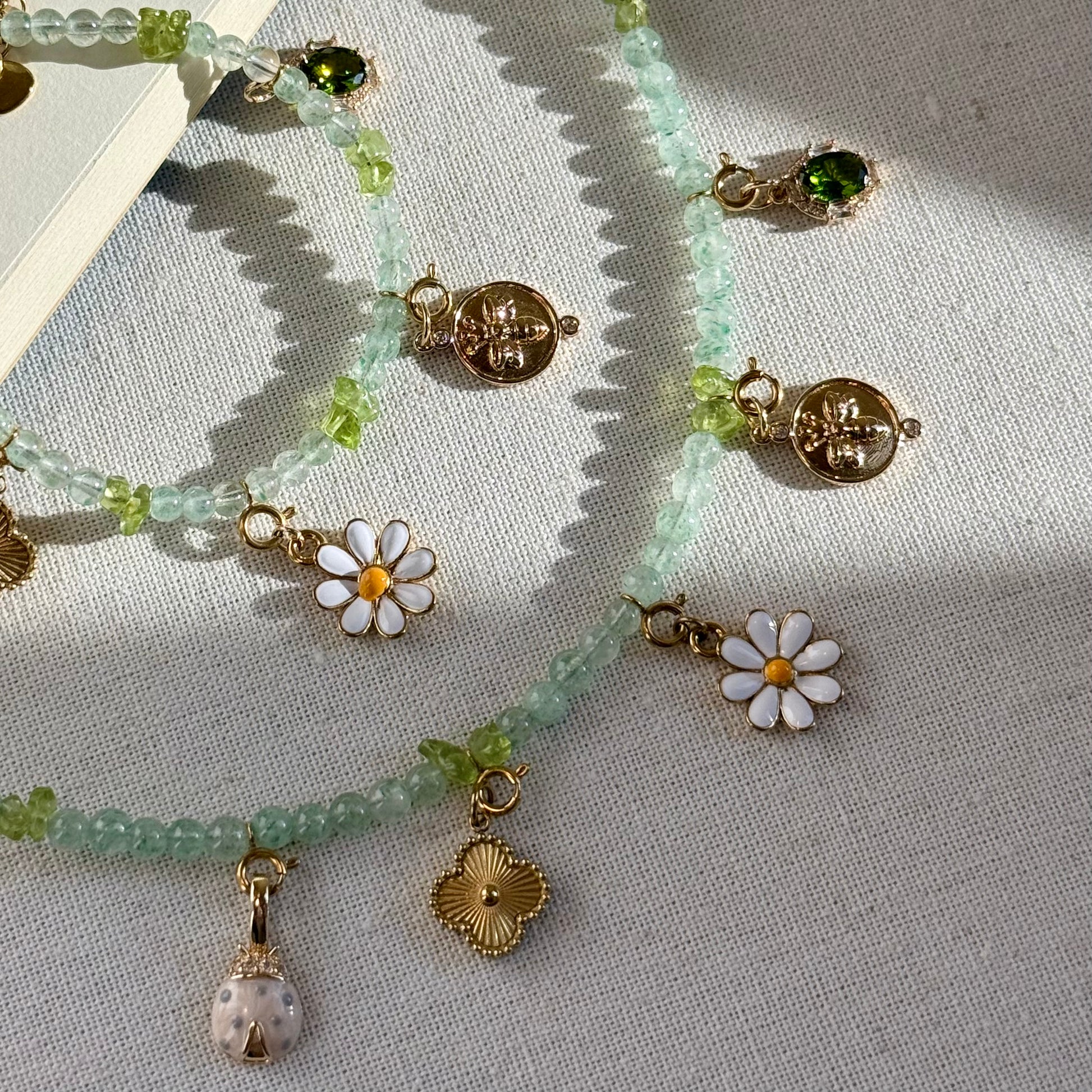Zoom-in Necklace and bracelet set with green beads and golden floral forest bee charms on a textured surface